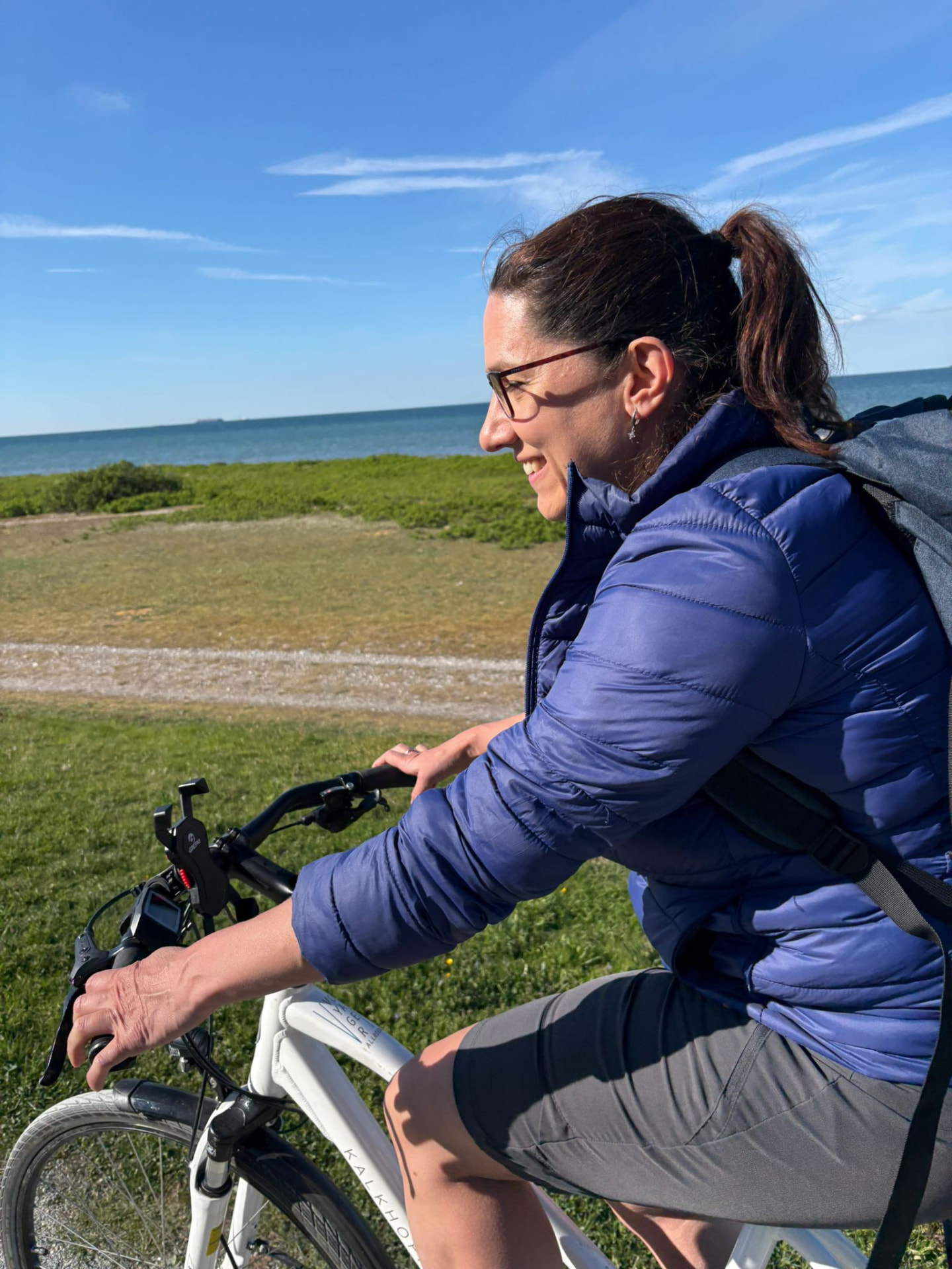 Susi Nocker fährt lachend mit dem Fahrrad an der Küste entlang